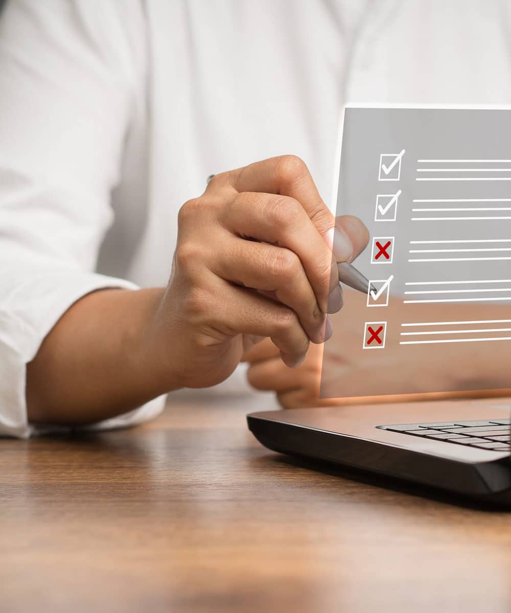 image of a man's hand holding a pen at a computer with a digital overlay of. checklist.