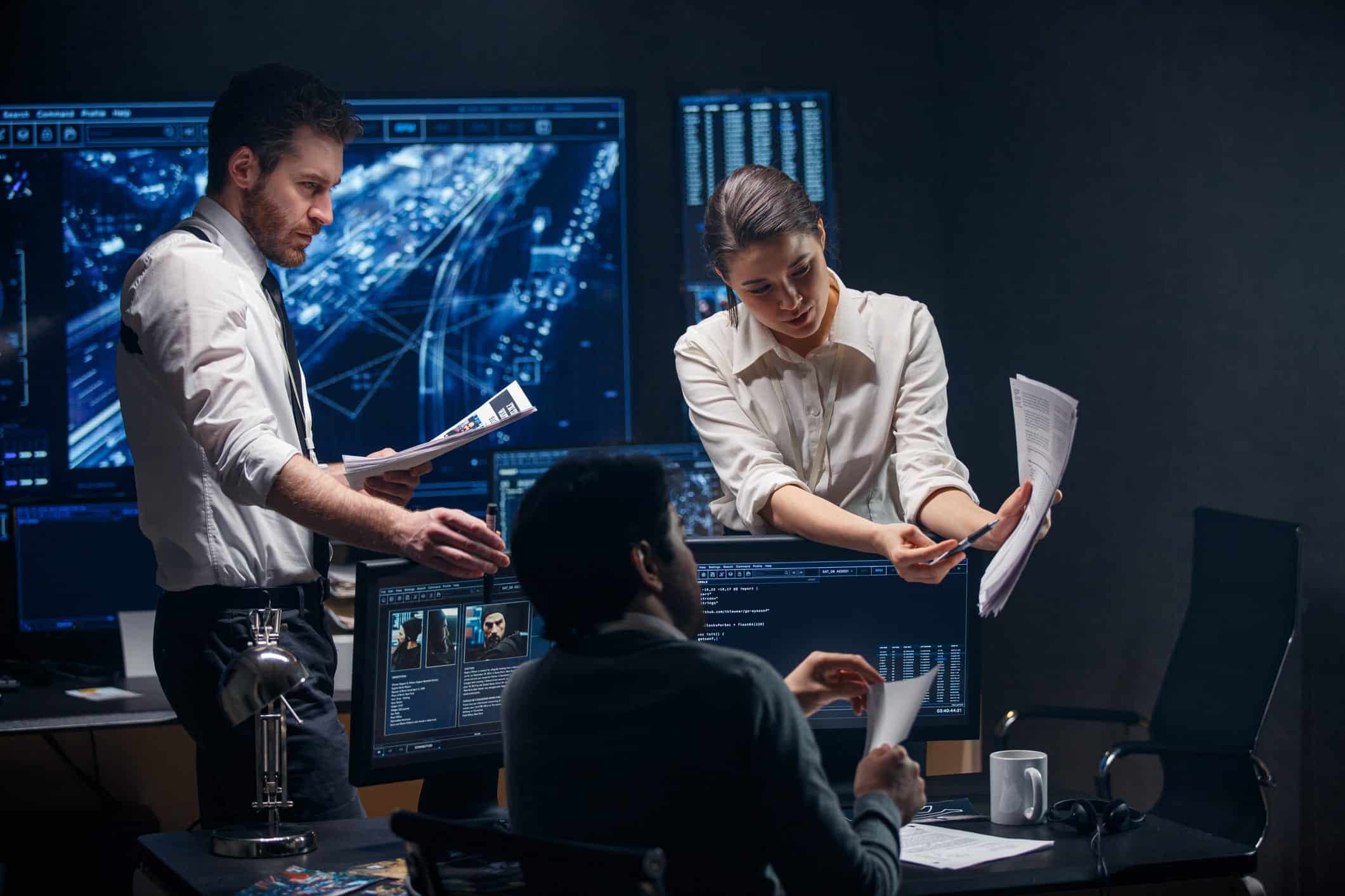government cybercrime workers analyzing information on computer screens and papers