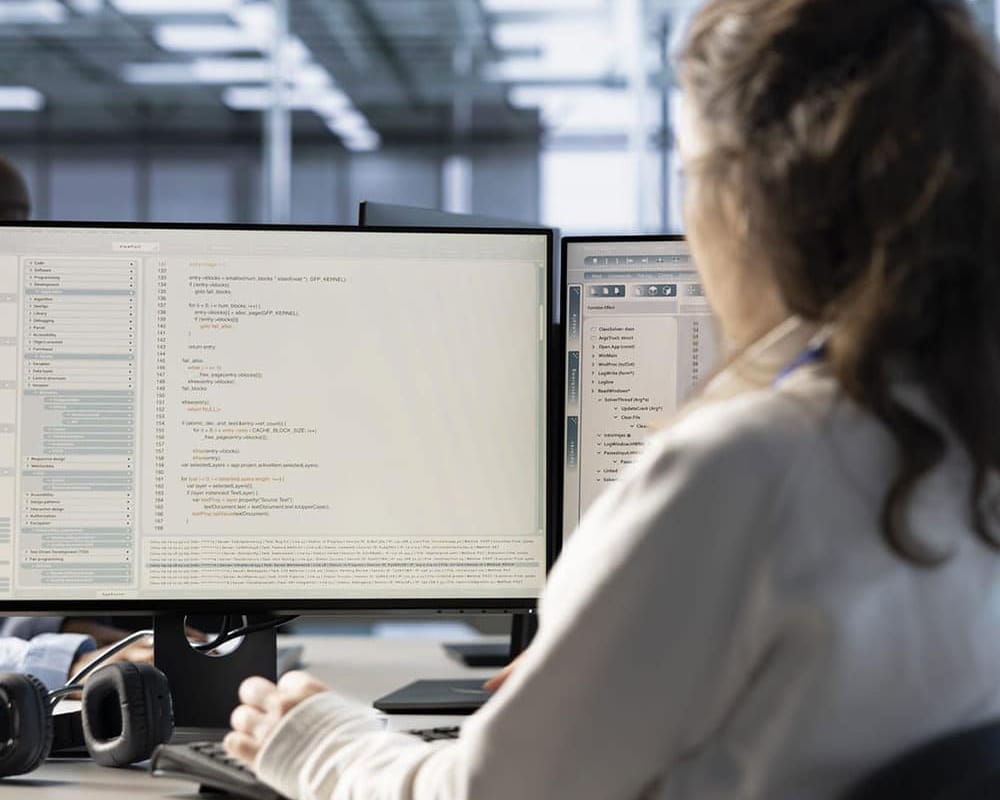 woman at computer with two displays, looking at data information