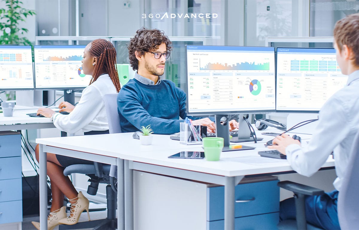 Modern open space office with business people working on desktop computers with graphs and charts in view