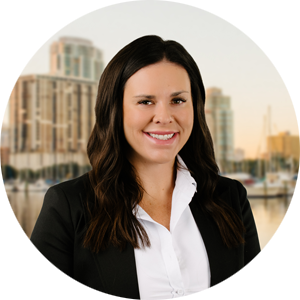 Professional headshot of a smiling woman in a white blouse and black blazer, with a city skyline and water in the background.