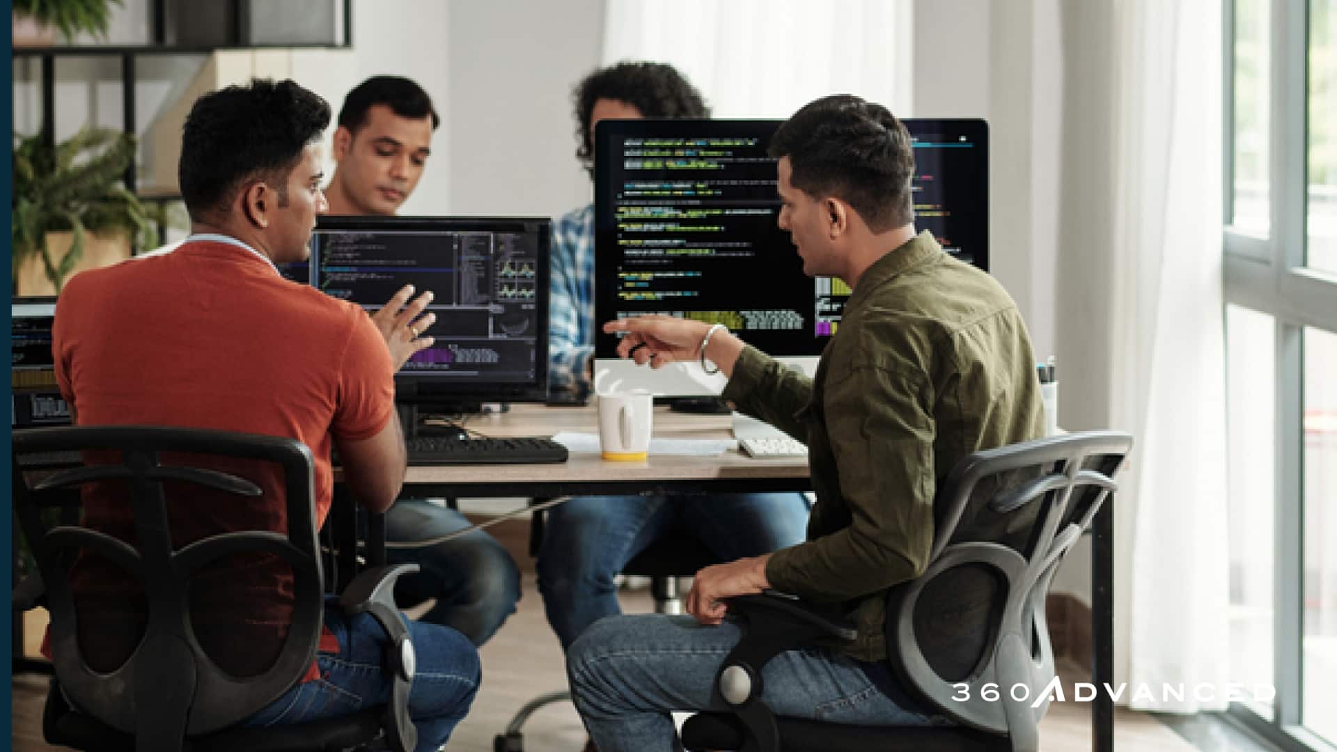 Developers discussing programming code in a pod of 4, sitting at desktop computers